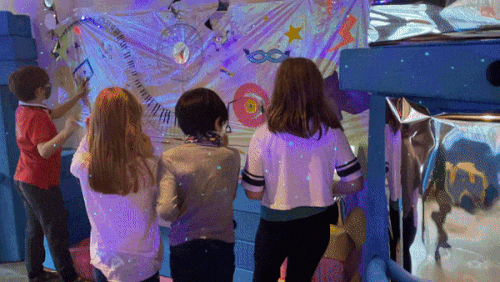 Four children stand in front of a colorful display.